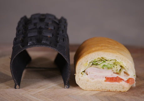 A sandwich next to a black food holder on a wooden surface.